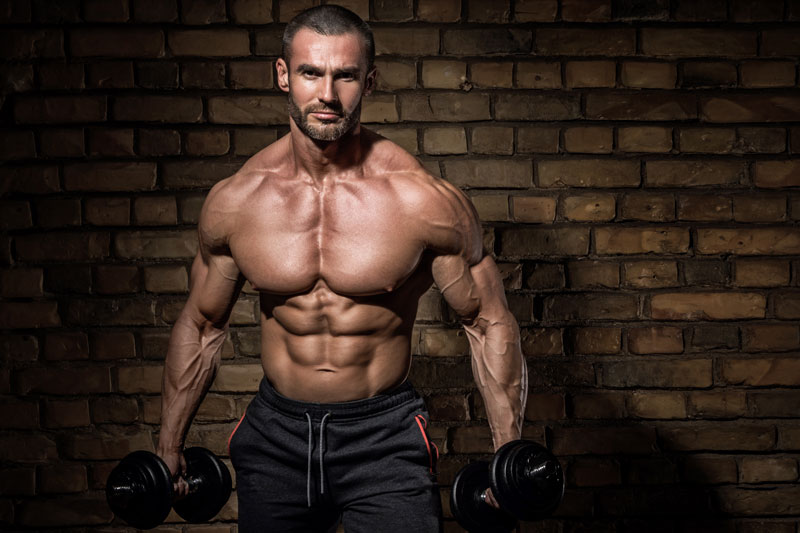 bodybuilder-doing-exercises with dumbbells against brick wall