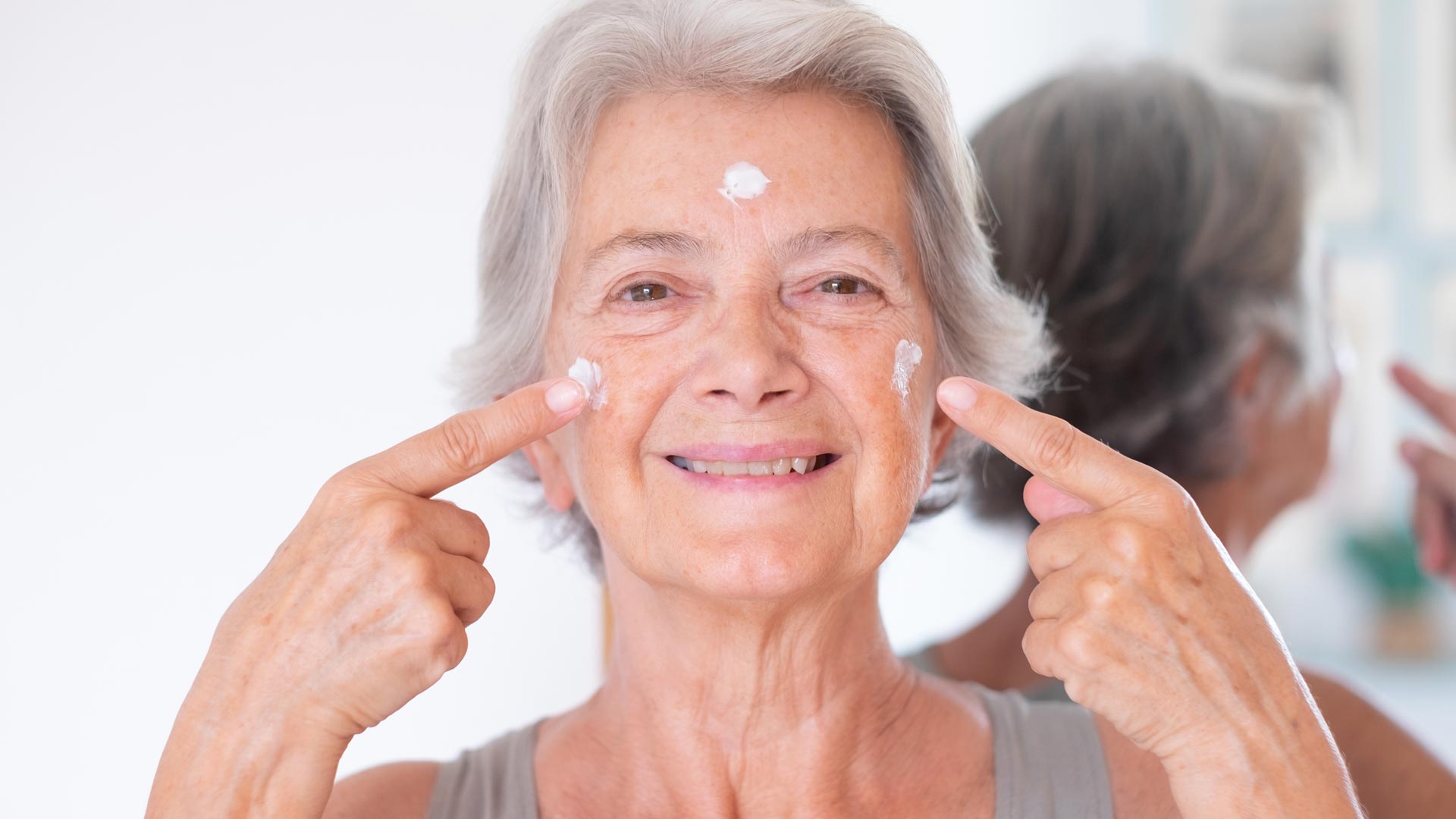 happy senior beautiful woman applies anti aging cream on wrinkled face
